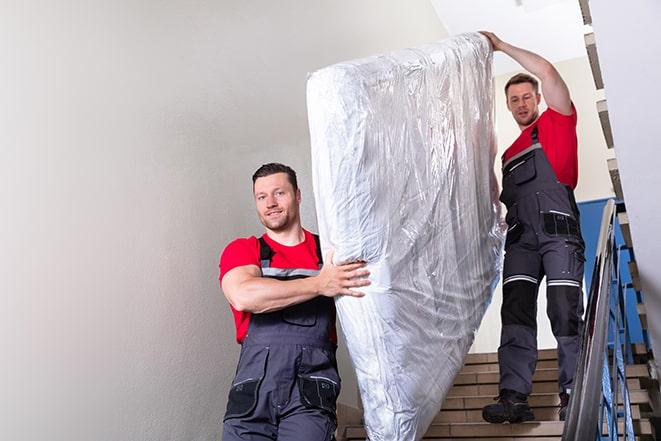 two workers carrying a heavy box spring out of a bedroom in Garden City MI